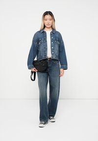 Τζάκετ από τζιν με μακριά μανίκια, ανοιχτού μπλε χρώματος, με κουμπί, συνδυασμένο με ψηλόμεσα σκούρα μπλε τζιν και μαύρη τσάντα χιαστί.