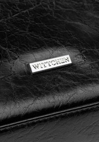 Czarny portfel z teksturowanej skóry, z metalową plakietką z logo "WITTCHEN" wytłoczoną na powierzchni. Widoczne szycie wzdłuż krawędzi. Gładkie wykończenie.