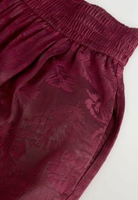 Bordeaux stof met een gladde, glanzende textuur met bloemenpatronen. Elastische tailleband met plooien aan de bovenkant voor volume.