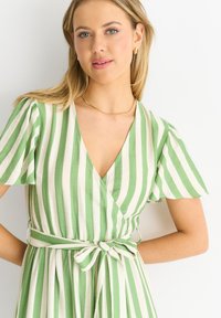 Green and white striped wrap dress with short flutter sleeves, a deep V-neck, and a tied waist, crafted from lightweight fabric.