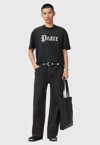 Fekete pamut póló fehér "Peace" grafikával, laza fekete farmernadrággal, fekete övvel és texturált fekete táskával párosítva.