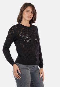Maglione nero lavorato a maglia con un motivo a losanga testurizzato, maniche lunghe e scollatura a girocollo. Abbinato a jeans in denim grigi per un contrasto.