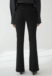 Jeans negros de campana hechos de denim, con un talle alto, dos bolsillos traseros y una textura suave. Los bordes están bien terminados.