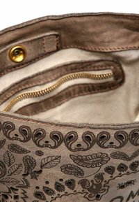 Interno di borsa marrone con texture, embossing floreale, tasca con zip dorata e fodera beige. Presenta una chiusura a scatto e cuciture decorative.