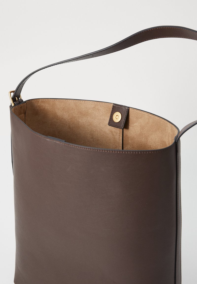 Braune Lederhandtasche mit glatter Außenfläche, weichem Wildlederinnenraum, schlichtem Design und langem Schultergurt. Sichtbarer sicherer Druckknopfverschluss.