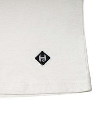 Hvid bomulds t-shirt med en afrundet bund, der har et sort diamantformet patch med et stiliseret bogstav "R" og topakcent.