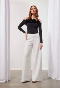 Black off-the-shoulder bodysuit with floral detail at neckline, paired with high-waisted, wide-leg white trousers and black sandals.