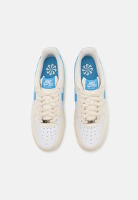 Tenisky Nike Air Force 1 s krémovým svrškem a modrými akcenty, perforovanou špičkou a světle modrou stélkou s květinovým vzorem.