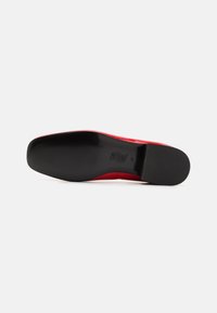 Red patent leather shoe with a smooth, shiny surface and a black rubber sole. Features a rounded toe design and minimalistic heel.
