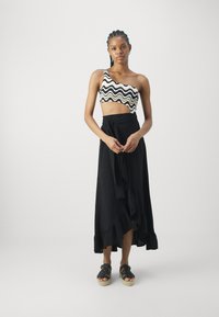 Eén-schoudertop met een zwart-wit golvend patroon, gecombineerd met een lange zwarte rok met een rucheszoom. Model draagt espadrilles.