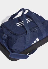 Námornícky duffel vak vyrobený z odolnej tkaniny. Obsahuje biele vodorovné pruhy, dvojité rukoväte a čierny základ. Zapínanie na zips na vrchu.