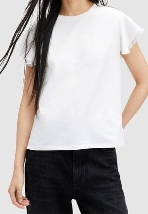 White cotton t-shirt with short ruffled sleeves, crew neck, and a relaxed fit. Paired with dark denim jeans.