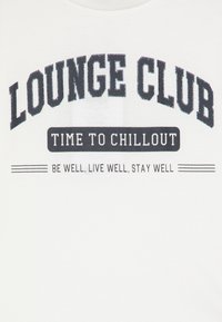 Camiseta blanca con un diseño gráfico audaz. El texto incluye "LOUNGE CLUB" en azul oscuro con un acabado brilloso sobre "TIME TO CHILLOUT" en negro.