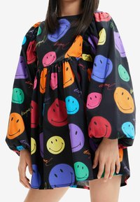 Czarna sukienka z kolorowymi wzorami uśmiechniętych buziek w odcieniach pomarańczowym, różowym, zielonym, niebieskim i fioletowym, z bufiastymi rękawami i marszczoną talią.