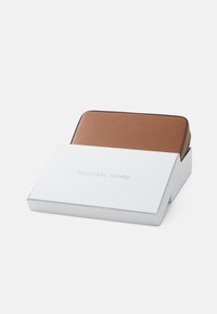 Billetera de cuero marrón con textura de guijarro y detalle en cremallera dorada, descansando en una caja blanca con "MICHAEL KORS" impreso en la tapa.