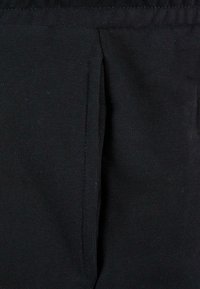 Black fabric features a smooth texture with visible stitching. Side pocket detail is highlighted, blending seamlessly with the material.