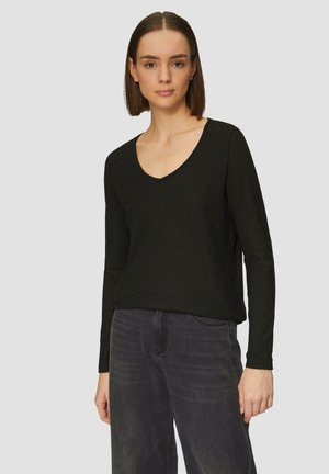 Top noir à manches longues avec un décolleté en V, fabriqué à partir d'un matériau doux, associé à un jean large gris foncé. Simple et polyvalent.