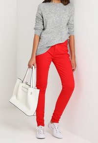 Suéter gris de punto, jeans skinny rojos, zapatillas blancas y un bolso blanco con acentos negros. Diseño simple con un look casual.