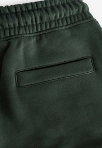 Donkergroene sweatpants met een elastische tailleband, zachte textuur en een gestroomlijnde achterzak met een rechthoekige opening.