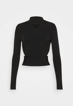 Top court à manches longues noir côtelé avec un col montant et une petite découpe en forme de clé sous le décolleté sur un fond blanc.