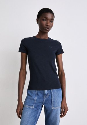 T-shirt a maniche corte blu navy in tessuto morbido con scollo rotondo, presenta un logo BOSS discreto sul petto. Abbinato a jeans azzurri.