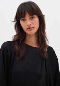 Blusa nera in seta con una vestibilità ampia, maniche lunghe e scollatura tonda; presenta una morbida trama e dettagli di drappeggio sottili.
