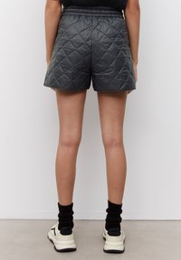 Shorts noirs matelassés avec une taille élastique, présentant un motif losange et une texture lisse, associés à des chaussettes montantes noires et des baskets.