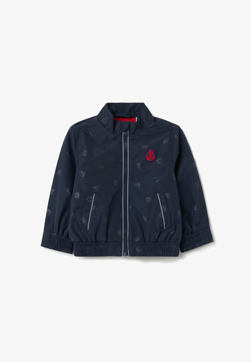 Giacca a vento navy con colletto rialzato, chiusura con zip, polsini elasticizzati e un motivo sottile di icone di barche a vela. Presenta un dettaglio del logo rosso.