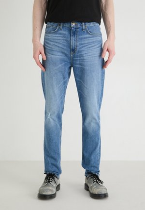 Light blue denim jeans feature a straight-leg design, subtle whiskering, and a small distressed area on the left knee.