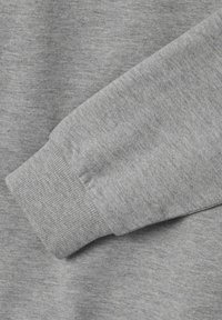 Tissu de sweat-shirt gris avec une finition texturée. Présente des poignets côtelés et un design doux et décontracté. Gros plan mettant en évidence les détails du matériau.