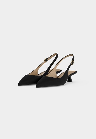 Paire d'escarpins slingback noirs à bouts pointus, petits talons kitten et brides de cheville à boucle dorée sur fond uni clair.