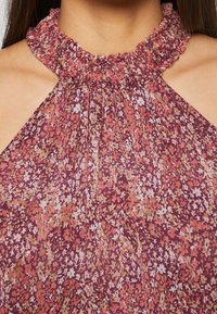 Nahaufnahme eines ärmellosen Blumenkleides mit einem hohen Rüschenausschnitt in den Farben Rosa, Lila und Beige.