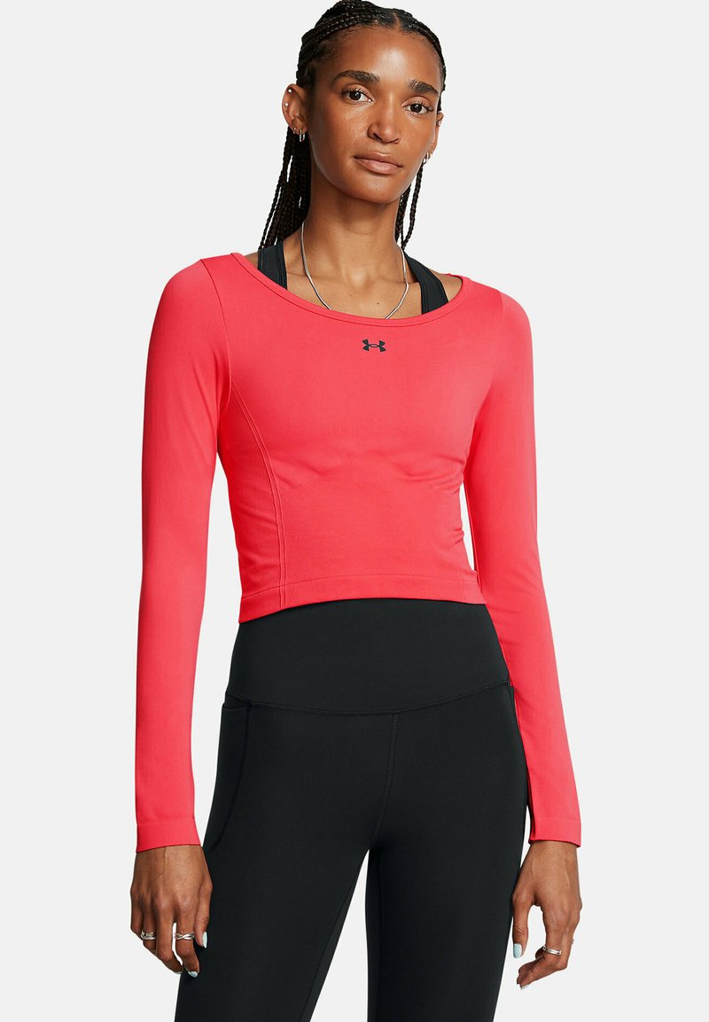 Pitkähihaatinen urheilu paita kirkkaan korallinvärisenä, istuva malli pyöreällä kaula-aukolla. Sisältää logon ja sileän tekstuurin, yhdistetty mustiin leggings-housuihin.