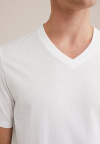 Vit t-shirt med v-ringning i mjukt bomullstyg. Korta ärmar, slät textur, subtil sömnad och klassisk passform. Passar för avslappnad användning.