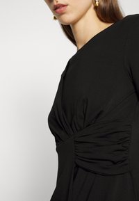 Czarna sukienka z dopasowanym górnym krojem, z marszczonym materiałem w talii, gładką fakturą i minimalistycznym designem.