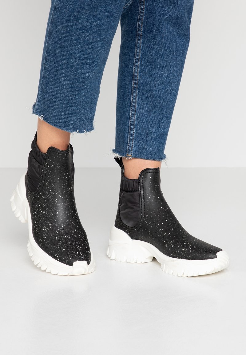 Bottines noires avec un motif à pois blancs et de grosses semelles blanches, portées avec un jean en denim bleu court.