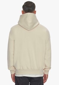 Beige kapuutsiga sweatshirt, mis on lõdva lõikega, ribatud mansetid ja äär. Pehme tekstuur, kujutatud tagantpoolt ilma täiendavate detailideta.