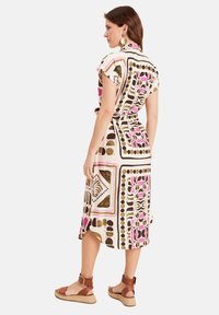 Korte mouwen midi-jurk in crème met geometrische patronen in roze, bruin en goud. Heeft een tailleband en flapkraag, en is gemaakt van een textuurstof.