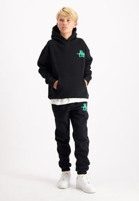 Zwarte hoodie en bijpassende sweatpants van zachte stof, voorzien van een groene grafische detail. De outfit heeft een losse pasvorm met zakken.