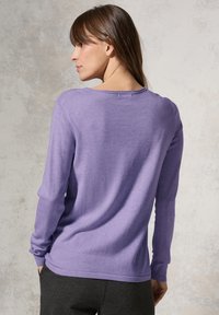 Fioletowa koszula z długim rękawem o luźnym kroju, okrągłym dekolcie i prążkowanych mankietach, wykonana z miękkiej, teksturowanej tkaniny, widok od tyłu.