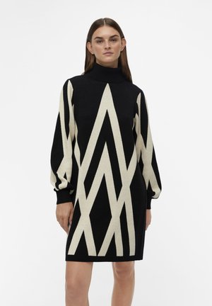 Abito lavorato a maglia in nero e crema caratterizzato da un collo alto, maniche rilassate e un motivo zigzag angolare su tutta la superficie.