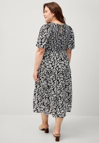 Schwarz-weißes Blumenkleid mit kurzen Puffärmeln, gerafftem Rücken und gestuftem Rock. Schlüssel-Ausschnitt hinten, kombiniert mit beigefarbenen Absatzsandalen.