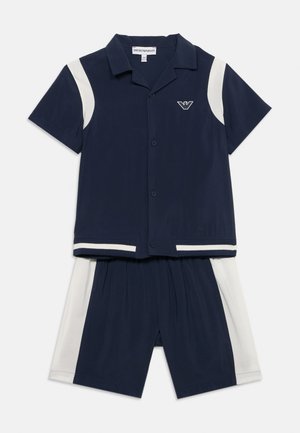 Tumesinist värvi lühikeste varrukatega nööpidega särk, valgete õlaaktsentidega, ning vastavad tumesinised lühikesed püksid valgete külgpaneelidega, Emporio Armani logo rinnal.