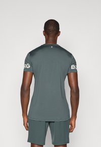 Gray athletic shirt with short sleeves, smooth texture, round neckline, and logo detail on the right sleeve, paired with gray shorts.