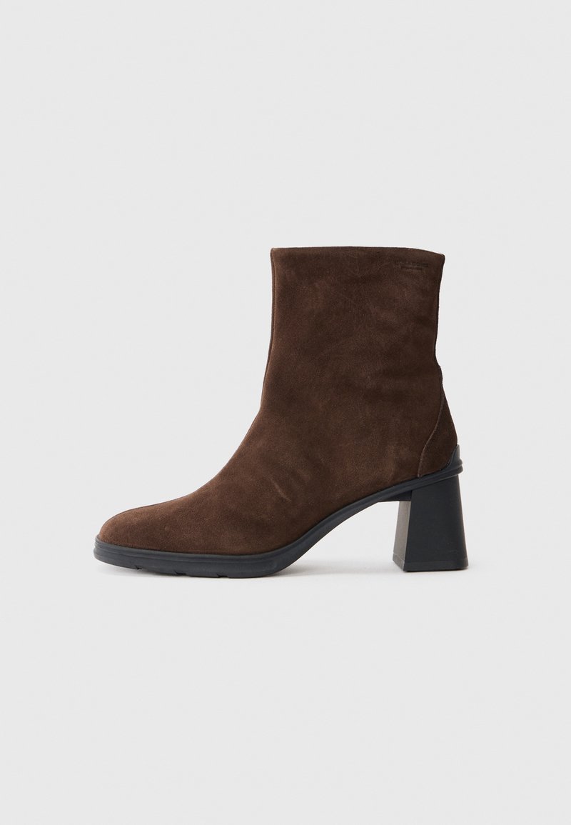 Bottine en suède marron avec un talon carré haut, un bout arrondi et une texture lisse. La bottine présente une silhouette moderne et élégante.