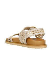 Geflochtene beige Sandale mit einer flachen, braunen Sohle, ausgestattet mit geflochtenen Riemen und einem runden Akzent. Offenes Design für Atmungsaktivität, strukturierte Oberfläche.