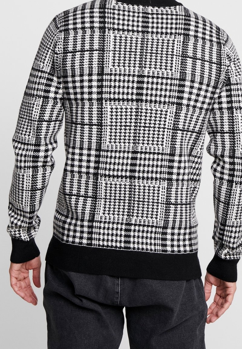 Schwarz-weißer karierter Pullover mit unterschiedlichen Mustern, gestrickter Textur, langen Ärmeln und einem schwarzen gerippten Bündchen und Saum.