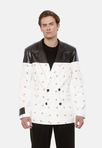 Podwójnie zapięta marynarka wykonana z białego materiału z czarnymi abstrakcyjnymi wzorami, z czarną skórzaną wstawką i mankietami oraz czarnymi guzikami.