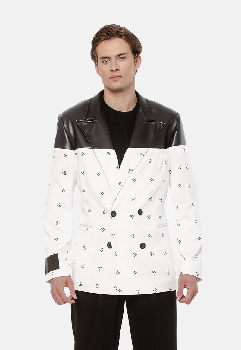 Podwójnie zapięta marynarka wykonana z białego materiału z czarnymi abstrakcyjnymi wzorami, z czarną skórzaną wstawką i mankietami oraz czarnymi guzikami.