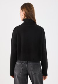 Schwarzer, kurz geschnittener Rollkragenpullover mit geripptem Kragen und Bündchen, weiche Textur, getragen mit ausgebleichten, grauen High-Waist-Jeans.